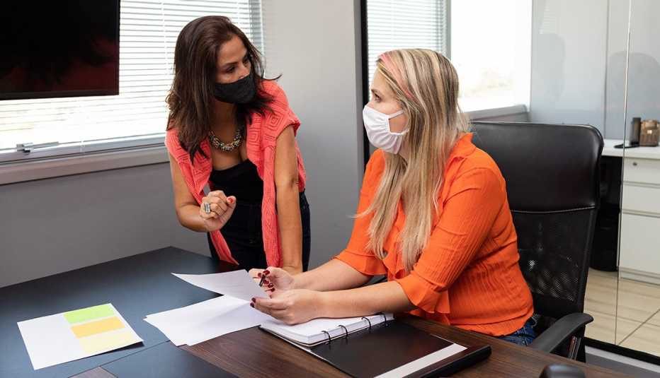 Dos mujeres usando mascarilla y hablando en una oficina