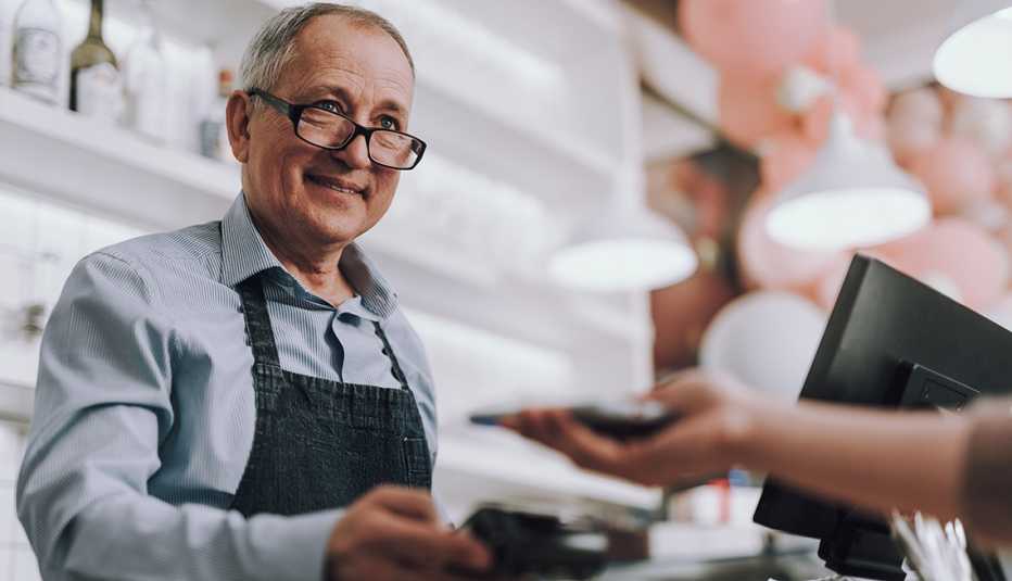 Hombre mayor trabajando como cajero en una tienda atiende a una cliente