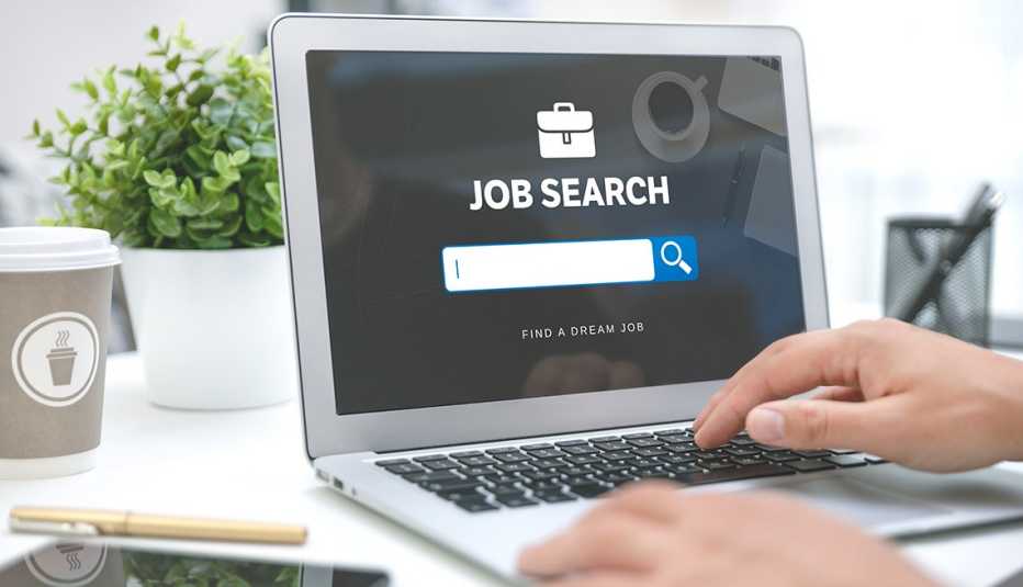 Manos de una persona sobre un computador en un escritorio que muestra en su pantalla un portal para búsquedas de trabajo