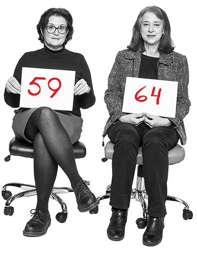 Julianne Taaffe, 59, y Kathryn Moon, 64, sentadas en sillas de oficina sosteniendo letreros con sus edades.