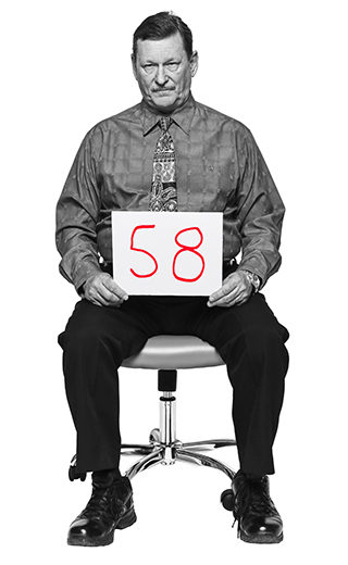 Walter Mikulan, 58, sentado en una silla de oficina sosteniendo en sus manos un letrero con su edad.