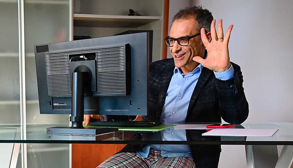 Hombre con pantalón de pijama, camisa y saco de corbata frente a una computadora.