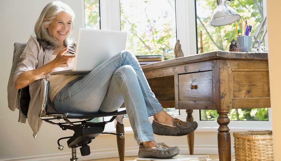Mujer sentada frente a su escritorio y con una computadora sobre las piernas.