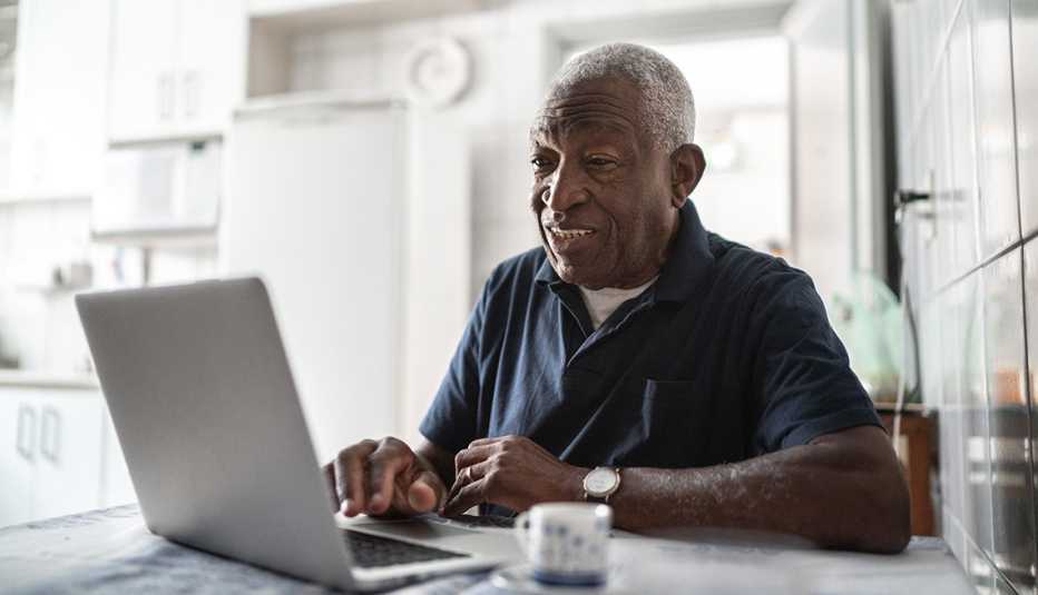 Hombre mayor sentado frente a una computadora en la cocina de su casa.