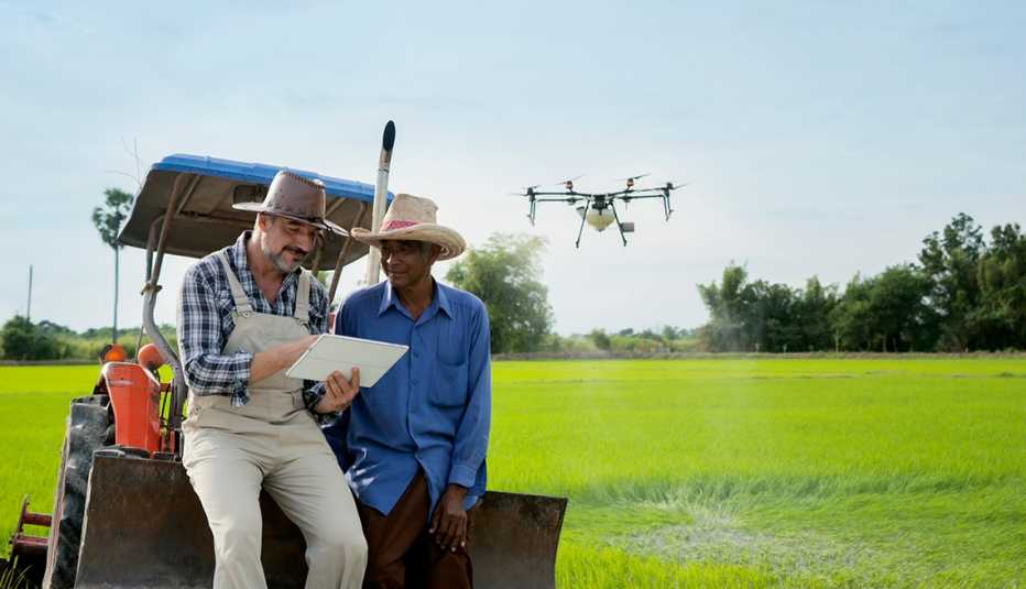 Dos hombres sentados en la parte trasera de un tractor pequeño operan un dron