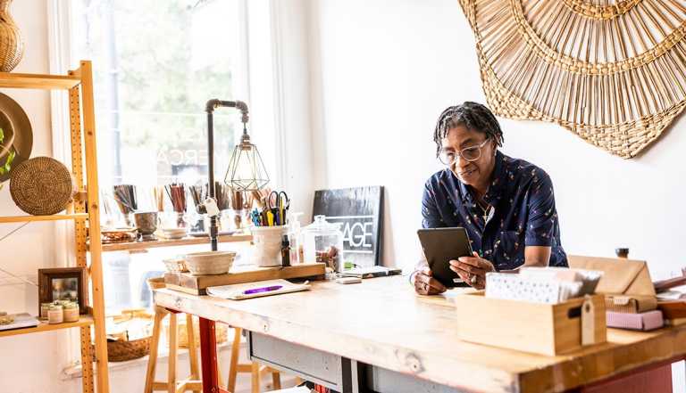 Mujer en su negocio mira una tableta y se apoya en su mesa de trabajo