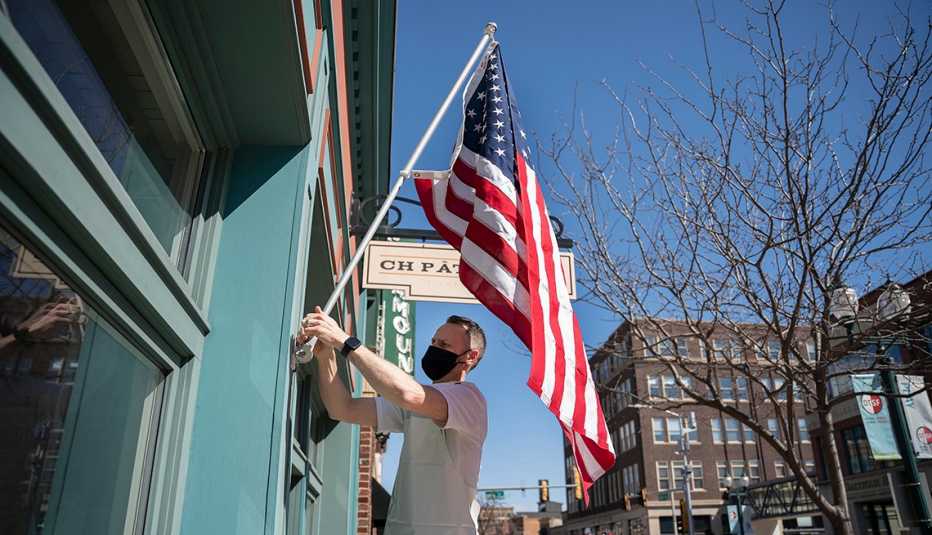 Chris Hanmer colocando una bandera de Estados Unidos a la entrada de su negocio, Ch Patisserie