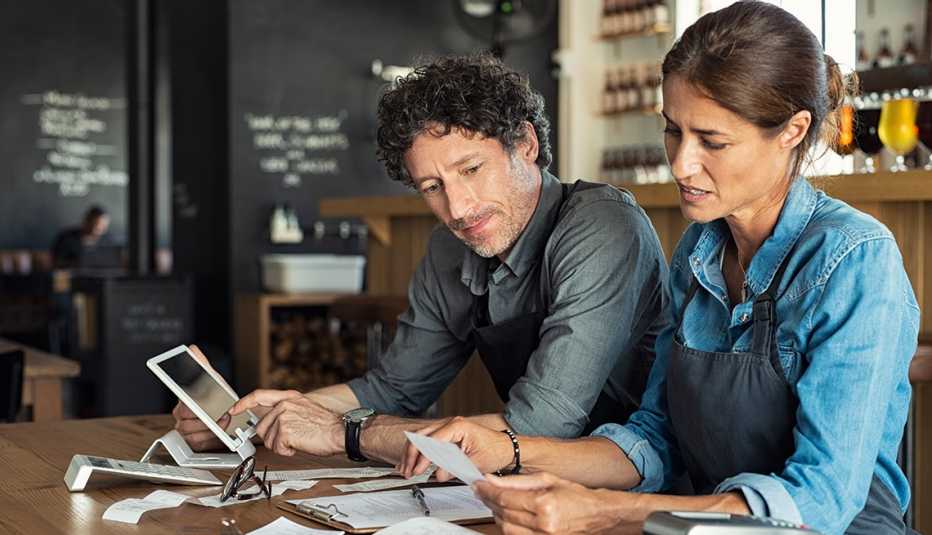 Hombre y mujer revisando las cuentas de su negocio en una de las mesas de su restaurante.