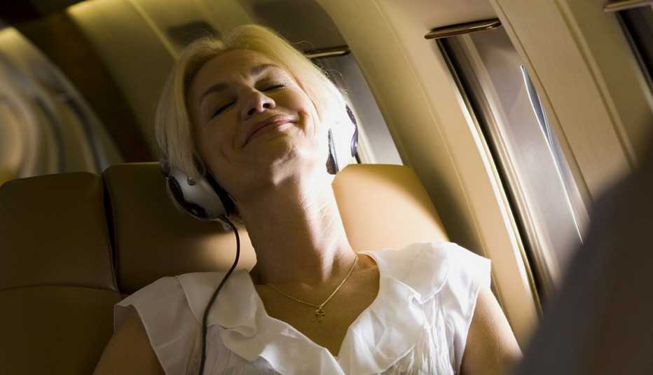 Mujer mayor usando unos audífonos en la silla de la ventana de un avión y las cosas que deberías saber antes de tomar un vuelo.