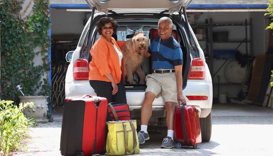 Pareja y su perro cargando maletas en un auto para ir de vacaciones