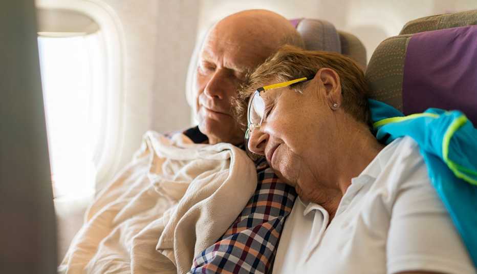 Pareja mayor de turistas durmiendo en el asiento de un avión.