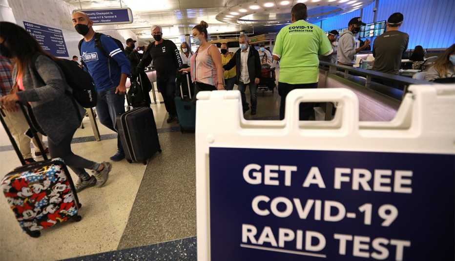 Viajeros pasan por delante de un letrero que les indica que obtengan una prueba rápida COVID-19 gratis
