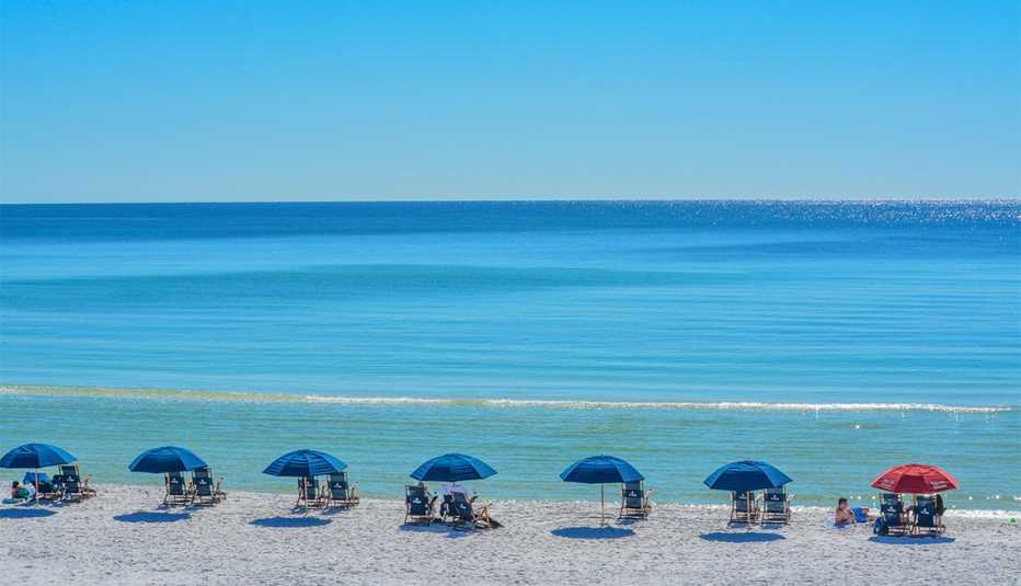 Personas en la playa con sombrillas y asientos en un día soleado