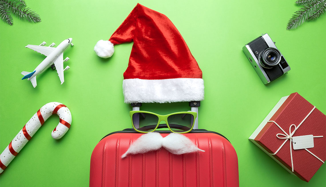 Una maleta con gafas de sol, bigote y un sombrero de Santa Claus, con un bastón de caramelo, un avión, un regalo de vacaciones y una cámara.
