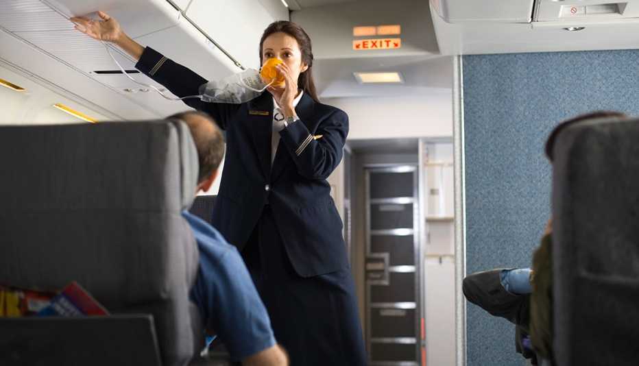 Azafata con una mascarilla ofrece instrucciones de seguridad en un avión