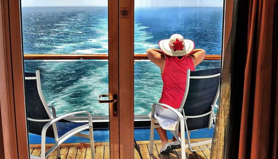 Mujer mira hacia el mar, mientras está sentada en el balcón de un crucero.