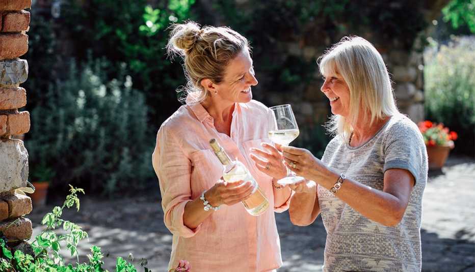 Dos mujeres maduras degustando una botella de vino blanco en sus vacaciones. Están de pie en el jardín de su Villa.