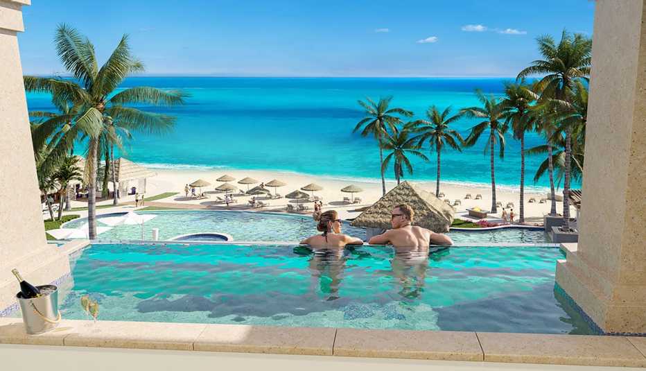 Dos adultos descansan en una piscina con vista al mar caribe