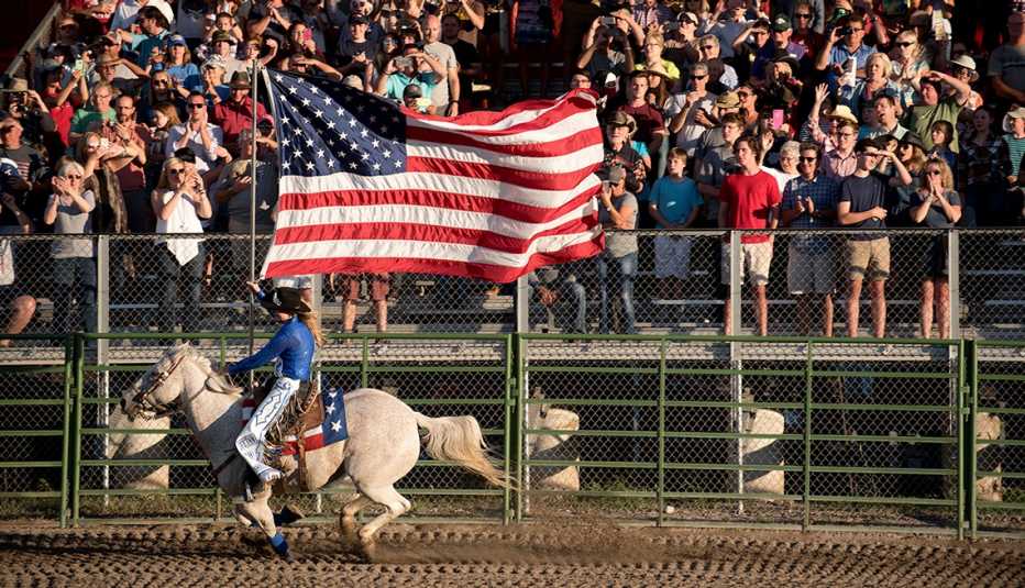 una participante de un rodeo lleva una bandera estadounidense mientras monta a caballo en un evento del 4 de julio en jackson hole