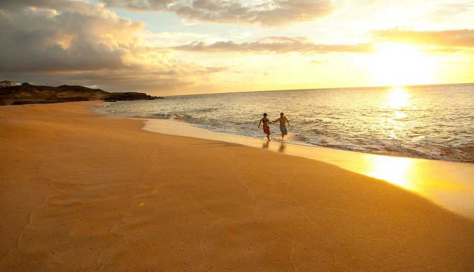 Dos turistas corriendo hacia el océano en la playa Papohaku, Moloka'i durante la puesta de sol