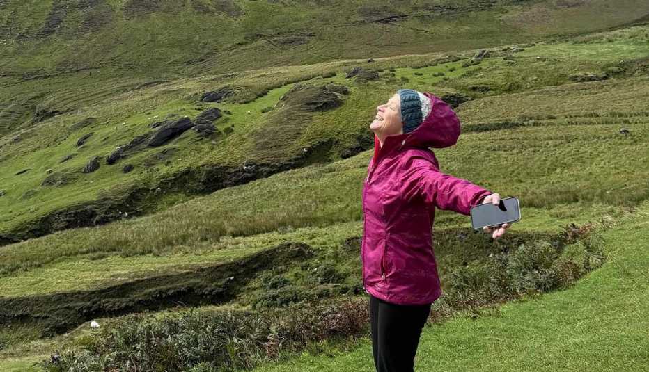 Older adult solo traveler enjoying a scenic countryside landscape while holding a smartphone outdoors