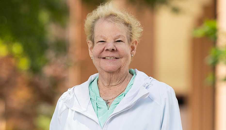 Outdoor portrait photograph of Heidi Griffin wearing a light-colored jacket and mint-green top, standing in front of a softly blurred garden and building background