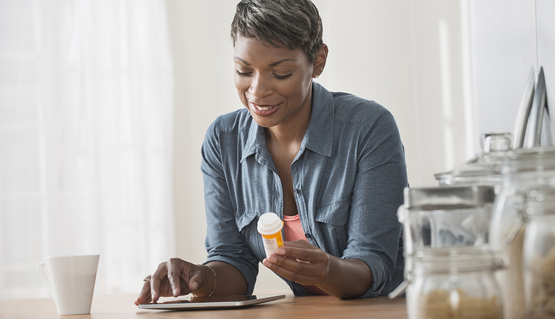 Una afroamericana sostiene en la mano izquierda un frasco de medicina mientras mira su tableta