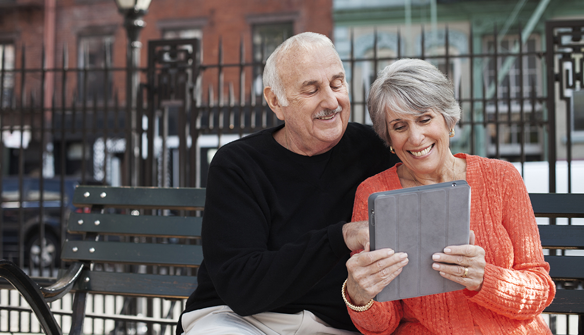 Una pareja de adultos mayores mira su iPad sentados en un banco en la calle