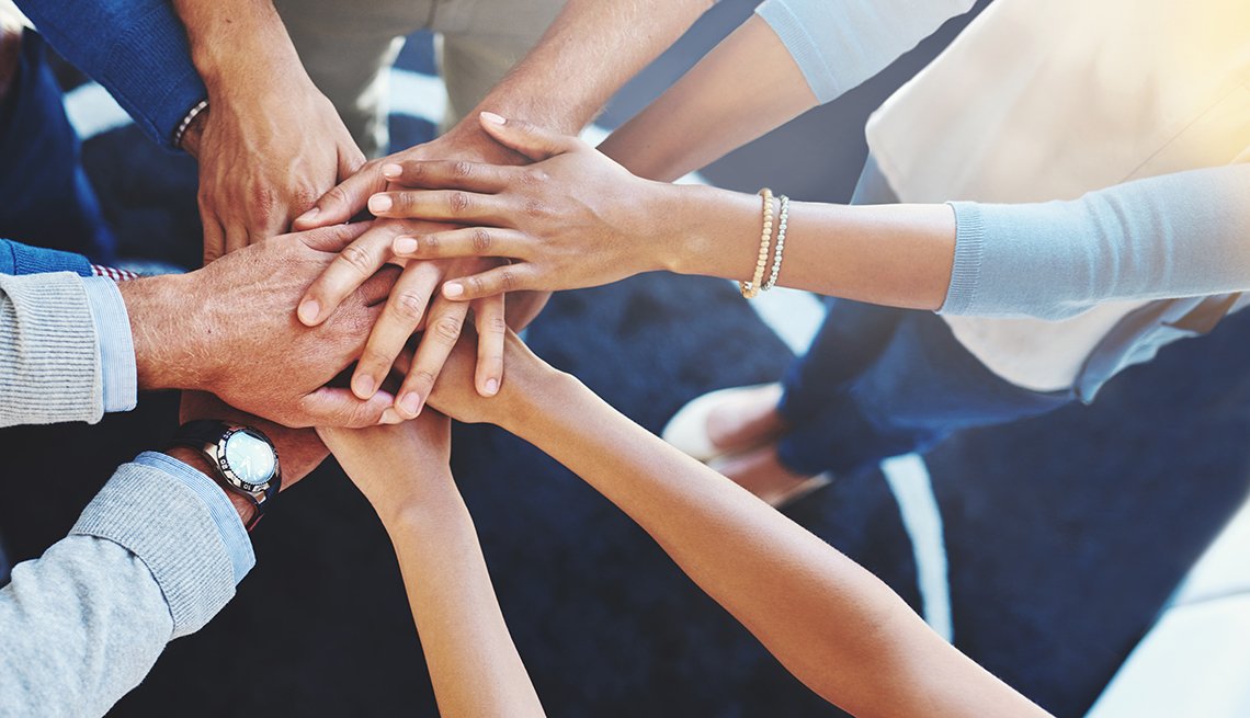 A multi-ethnic group of business people standing in a huddle with their hands together. AARP Foundation encourages people to help others recognize, refuse and report fraud by volunteering with the organization.