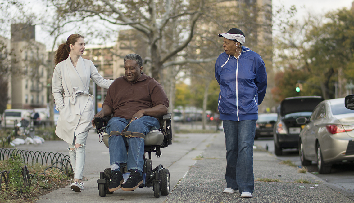 Two women walking down a city sidewalk with a man in a motorized wheelchair