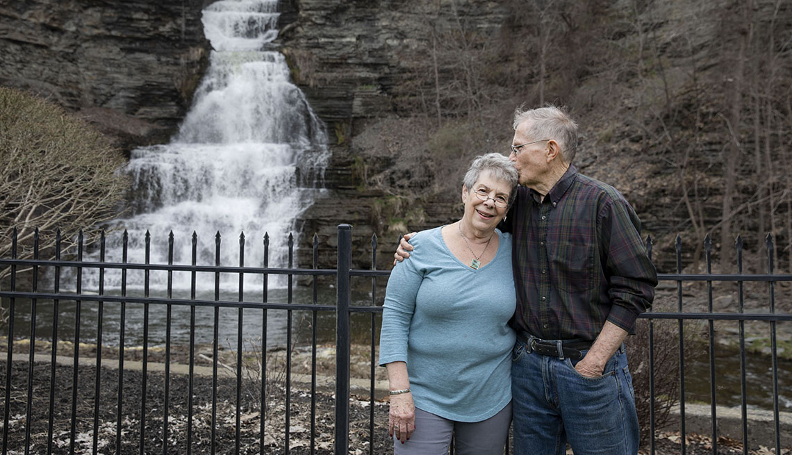 Man and woman hugging, pose in front of a waterfall