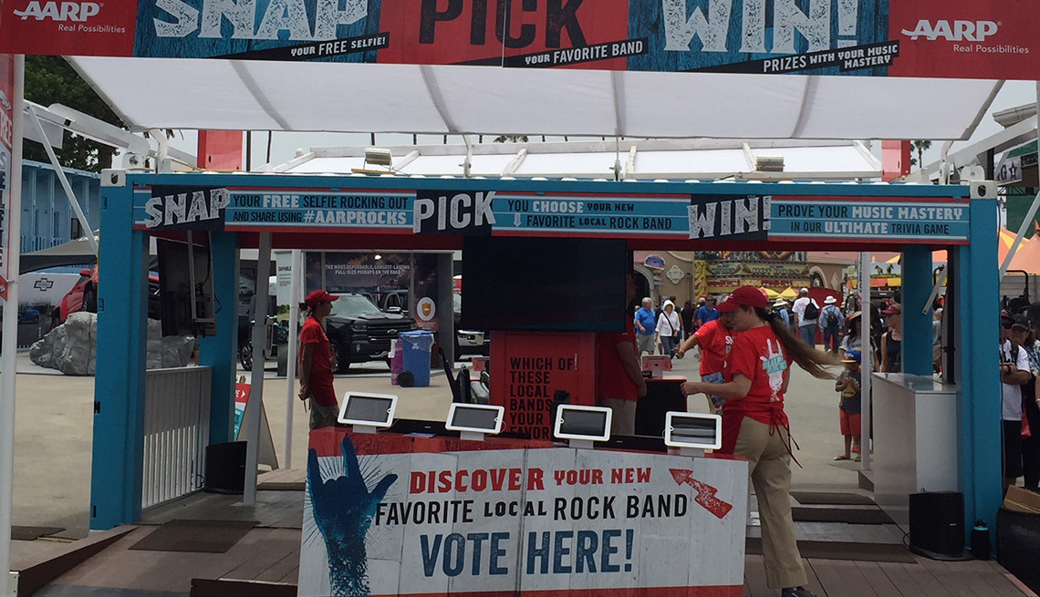 A A R P booth at a fair in San Diego, California. Sign in front says Discover your new favorite rock band. Vote here