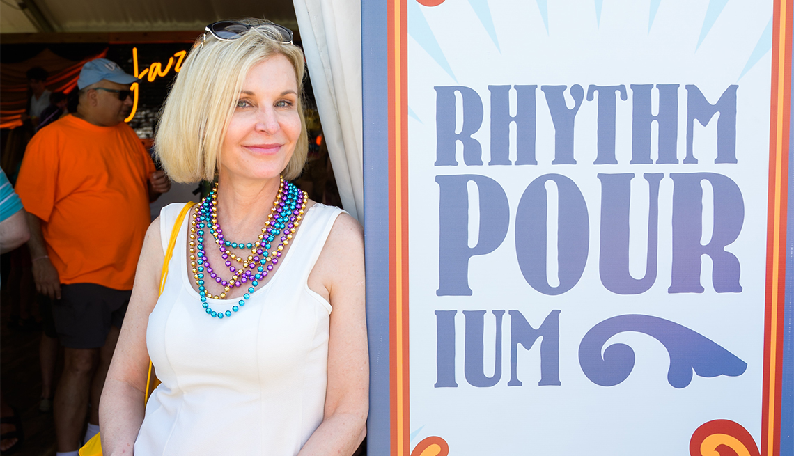 woman wearing mardi gras beads leaning agains a sign reading rhythm pour ium