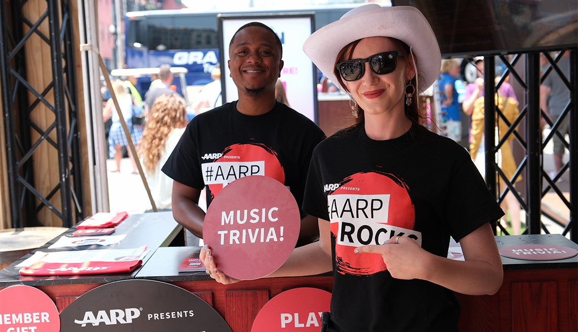 woman in a cowboy hat wearing a t shirt that says a a r p rocks and holding a sign that says music trivia