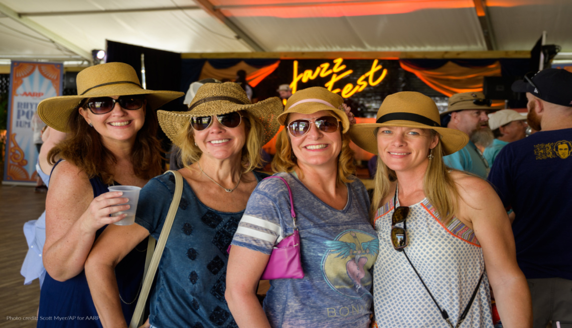 four women wearing hats in front of a jazz fest neon sign