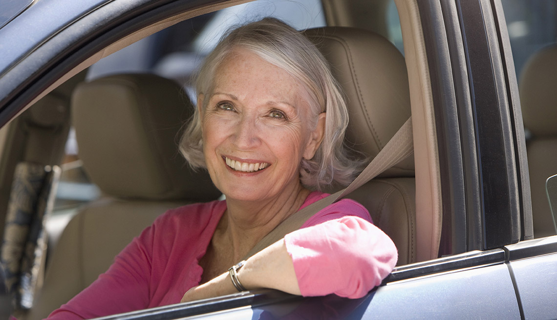 Mujer mayor sonríe mientras está sentada en un auto.