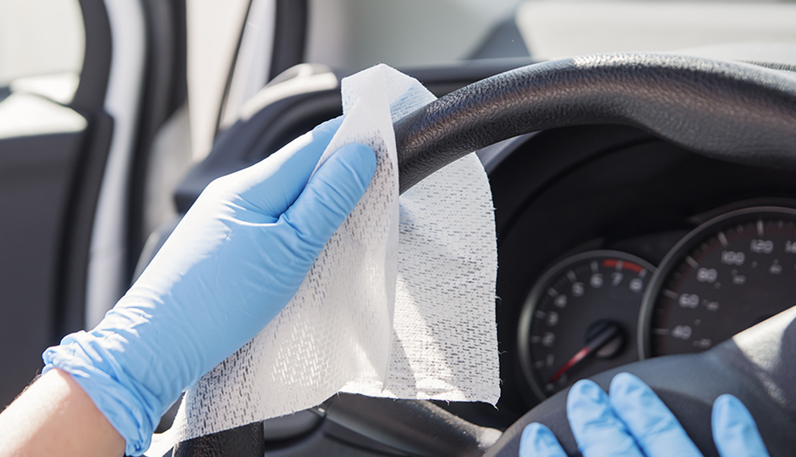 Female hands with blue glove wiping car steering wheel with disinfectant wipe. Horizontal outdoors close-up with copy space