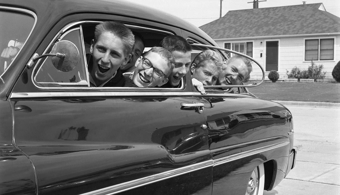 black and white photo taken in the nineteen fifties or sixties of five teenage boys all smiling and laughing peeking out the windows of their car
