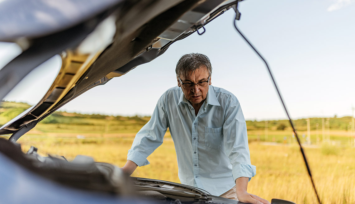 stressed man man leans over open hood of car checking engine after breaking down on the road