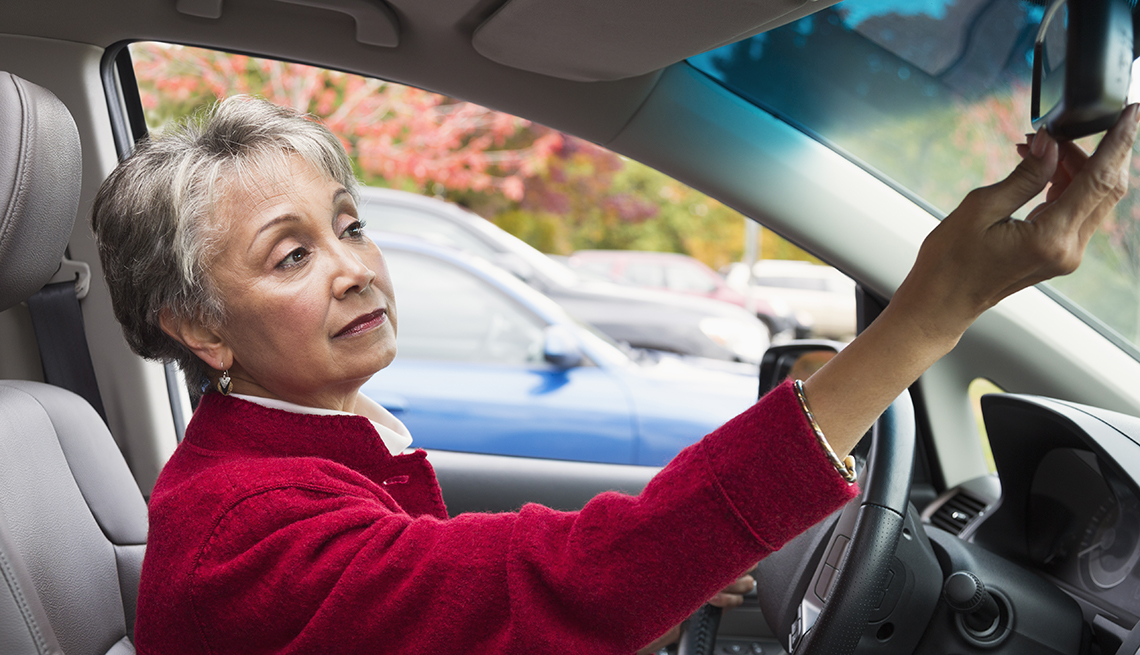 Mujer con una chaqueta roja ajusta el espejo de su auto