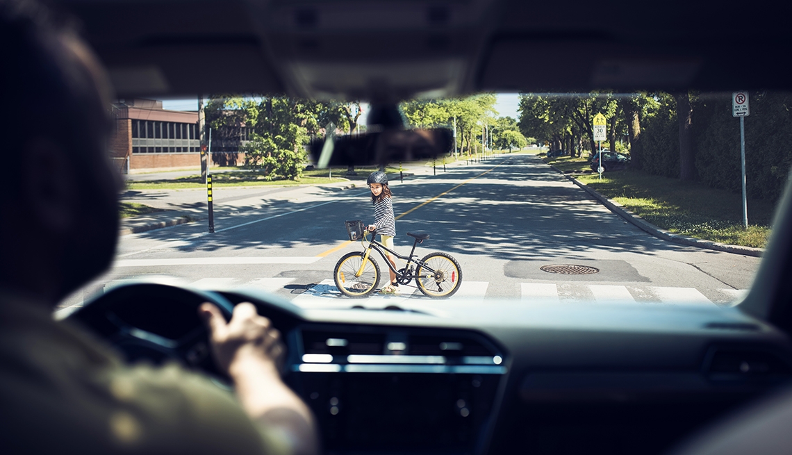 Conductor frena en un paso de peatones donde una niña cruza la calle caminando con su bicicleta