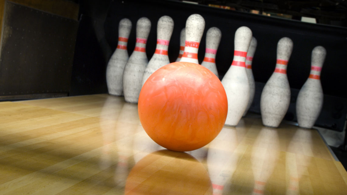 orange bowling ball in front of pins
