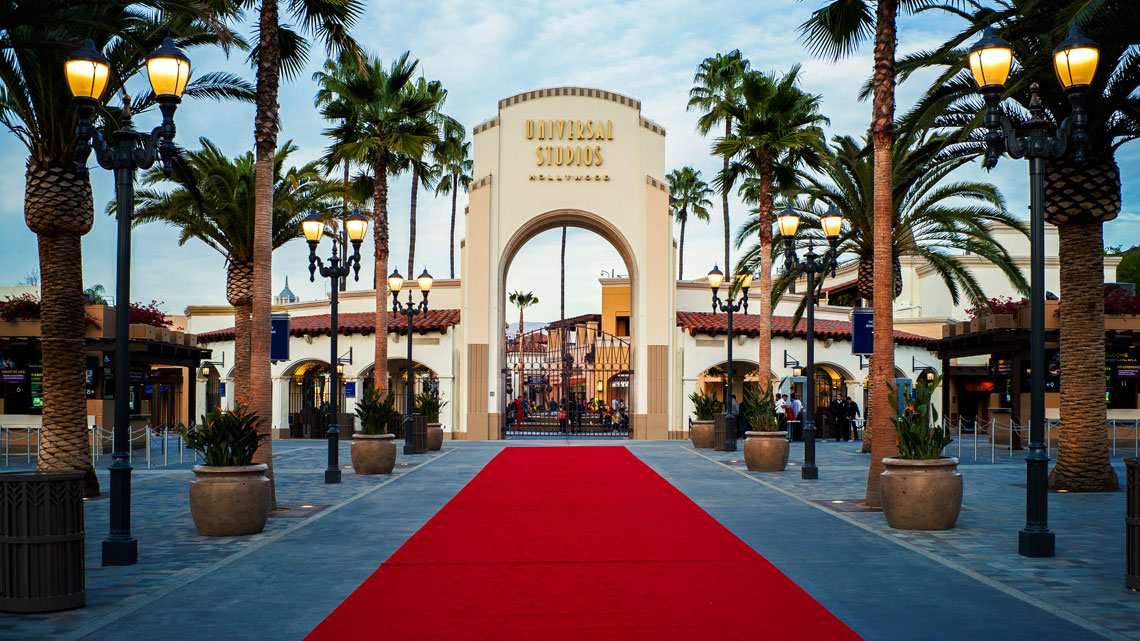 entrance with red carpet to Universal Studios Hollywood, palm trees, blue with clouds sky