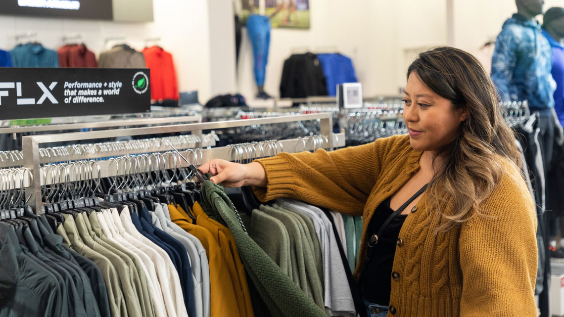 woman wearing mustard color cardigan sweater over black shirt looking through a rack of men's shirts in a store setting