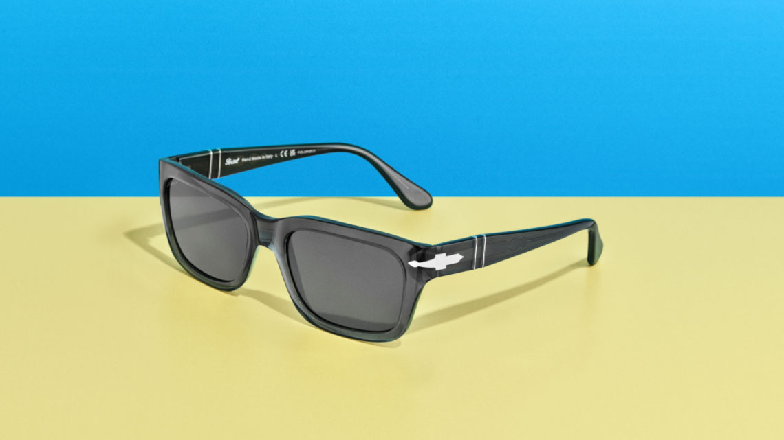 black pair of sunglasses with silver accents sitting on a yellow base with a blue background