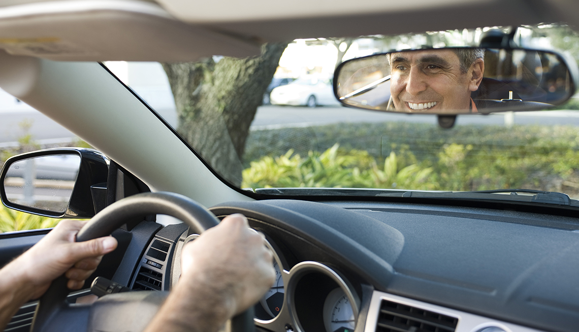 Un hombre sonriendo en su espejo retrovisor mientras conduce