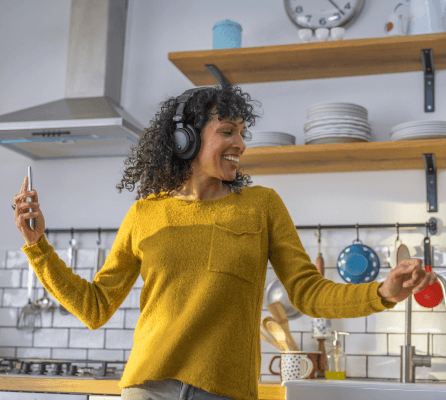 woman dancing in kitchen with headphones and cellphone wearing a yellow sweater