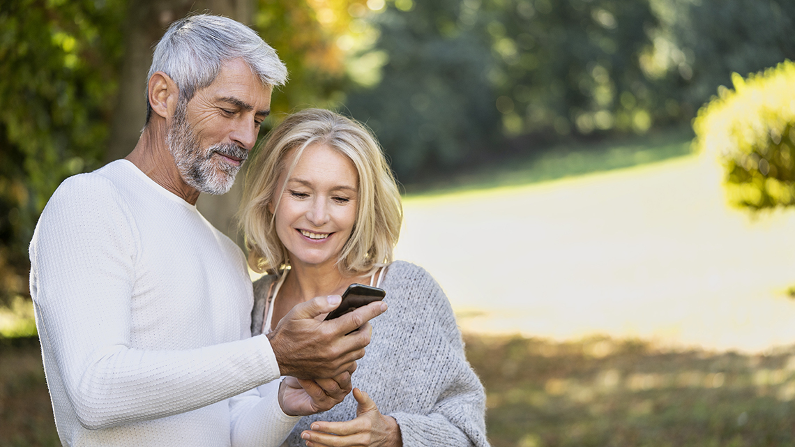 Smiling mature couple using smartphone while standing in backyard