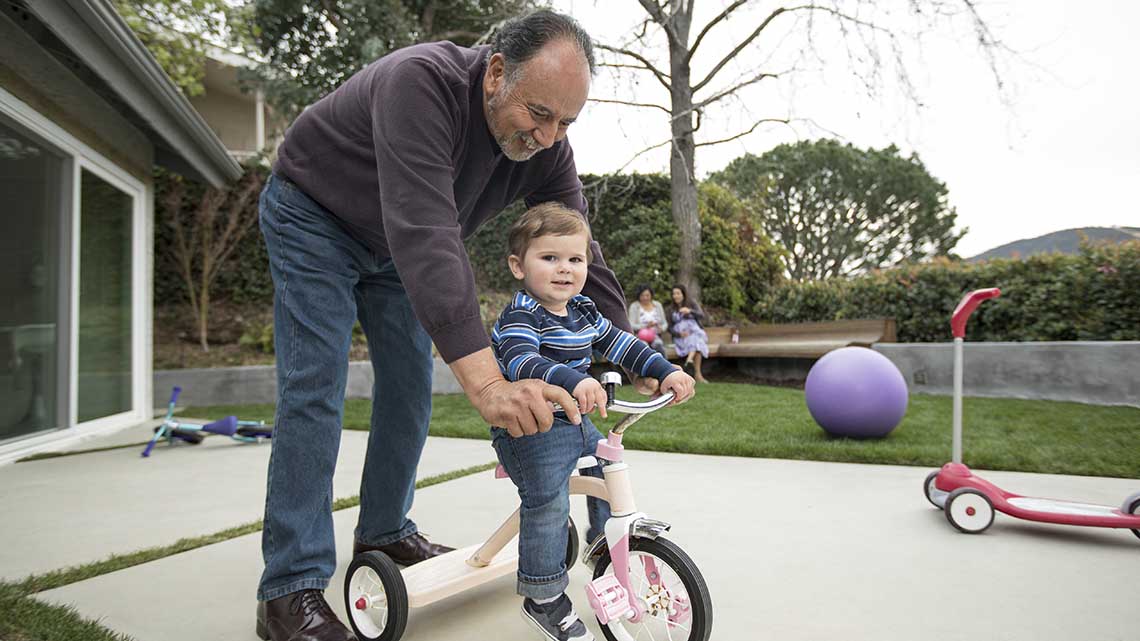 Grandfather pushing grandson on tricycle