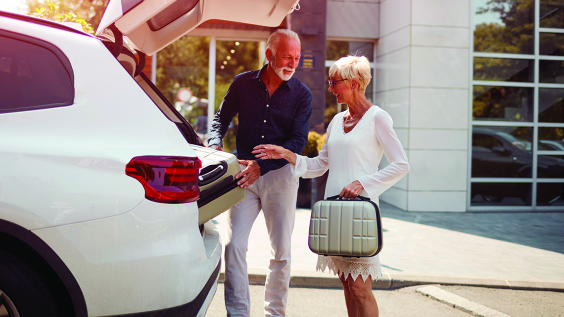 Mature man, woman loading suitcases into back white hatchback